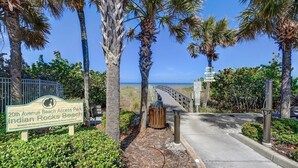 Schild für den 20th Avenue Beach Access Park Indian Rocks Beach, mit einem Weg zum Strand, umgeben von Palmen und blauem Himmel.