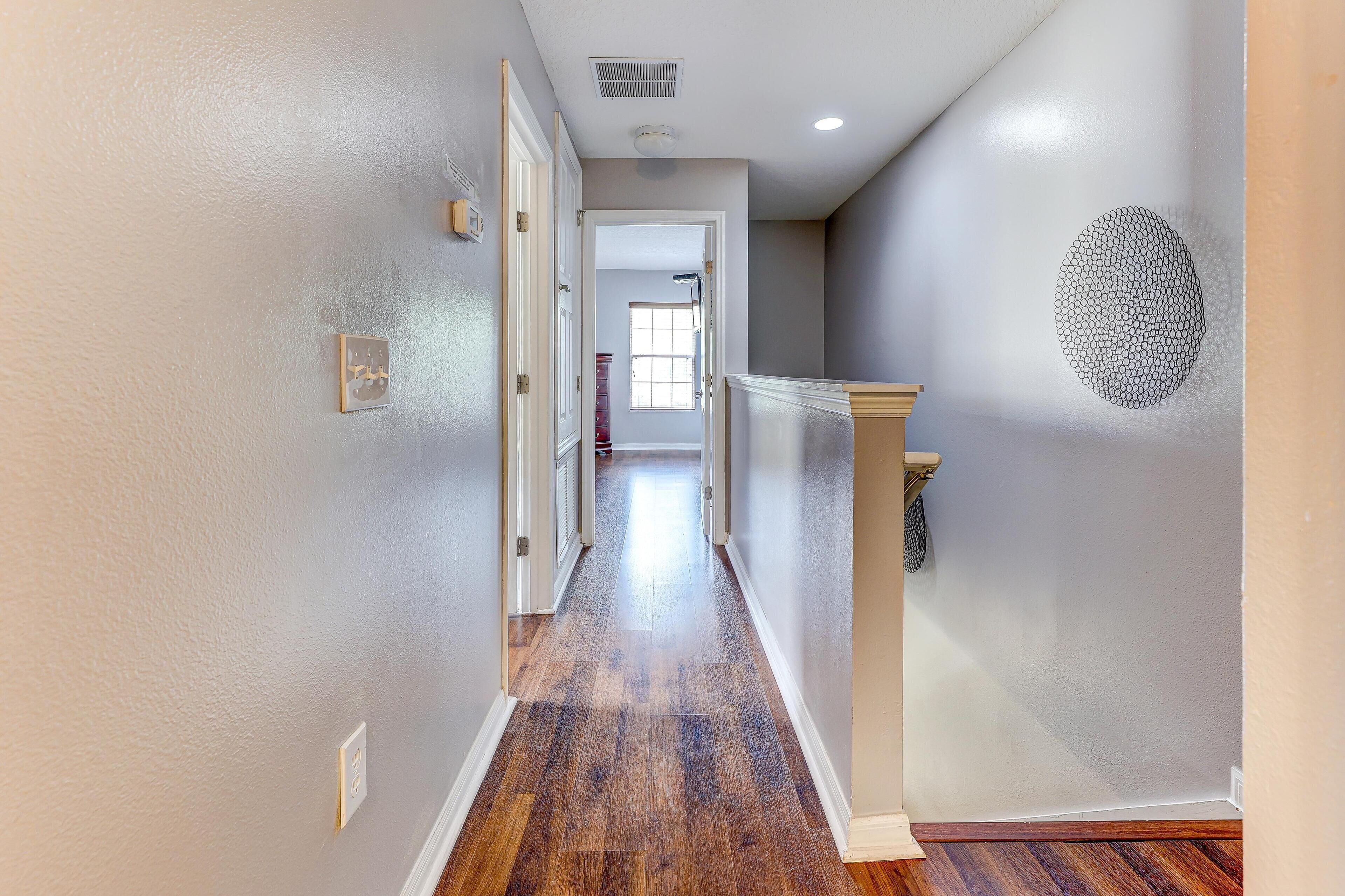 A hallway with wooden flooring, white walls, and a door leading to another room.
