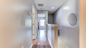 Un couloir doté d’un plancher en bois, de murs blancs et d’une porte donnant sur une autre pièce.