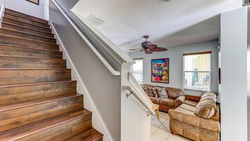 A wooden staircase leading to a living room with a ceiling fan, a sofa, and a window with blinds.