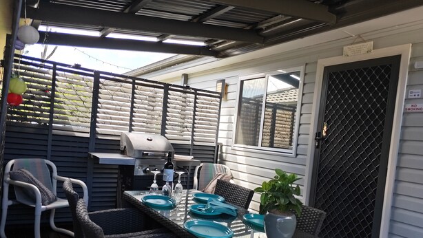 Une terrasse extérieure équipée d’un barbecue, d’une table à manger, de chaises et d’une plante en pot.