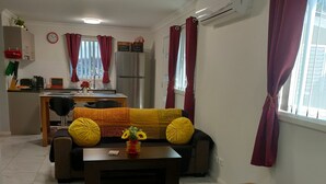 Un salon avec un canapé, une table basse et un tapis coloré. Il y a également un coin cuisine avec un réfrigérateur et une table à manger.