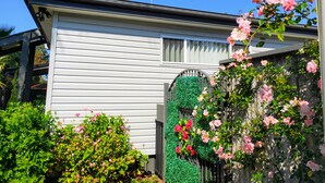 Une maison blanche avec une porte verte, entourée d’une végétation luxuriante et de fleurs roses.