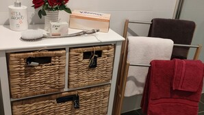 Une salle de bain avec un meuble-lavabo blanc, des paniers en osier, un porte-serviettes avec une serviette rouge, et des articles de toilette posés sur le comptoir.