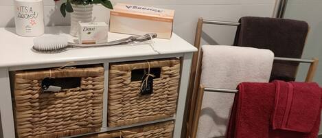 A bathroom with a white vanity, wicker baskets, a towel rack with a red towel, and toiletries on the counter.