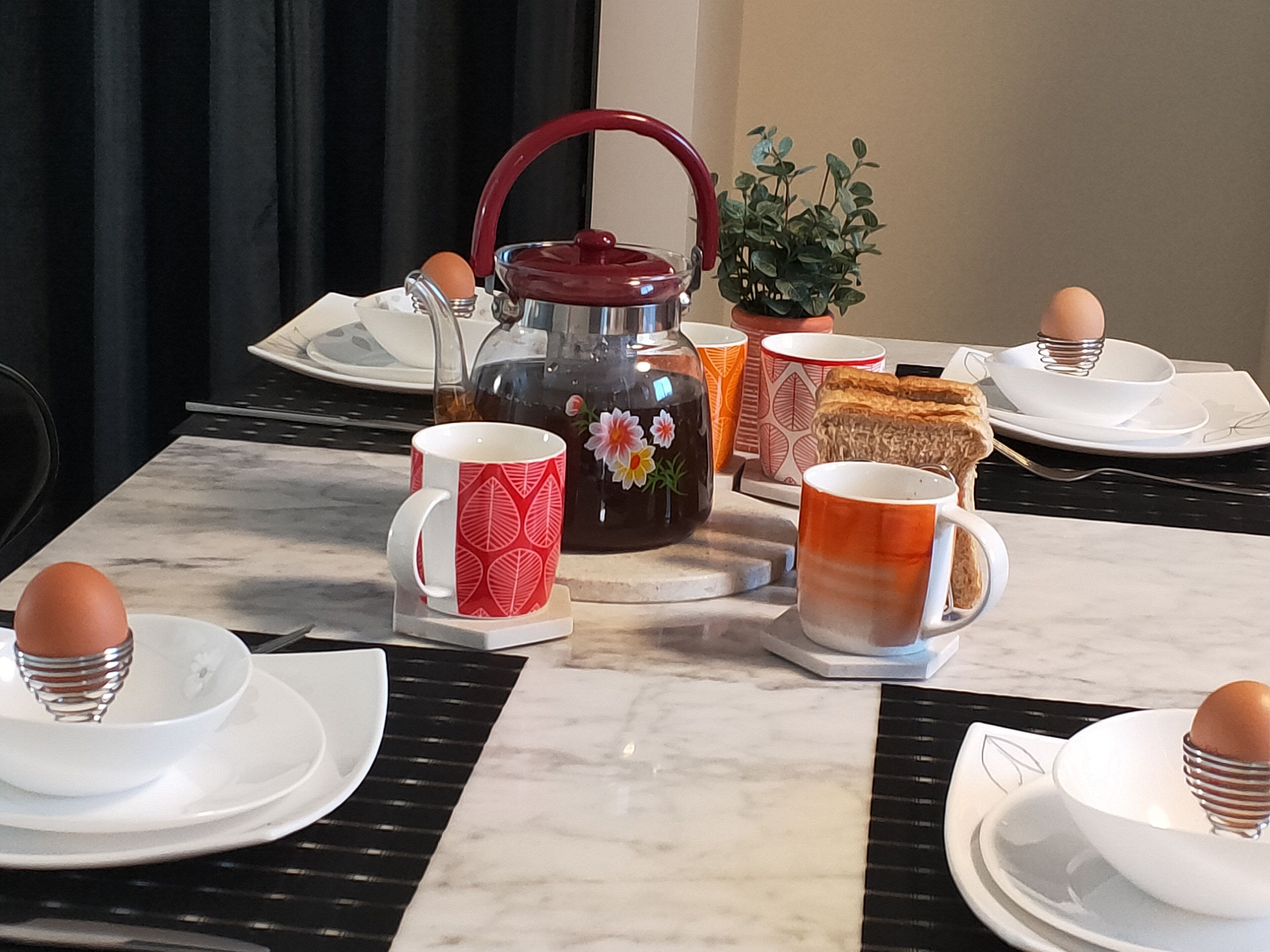 Une table en marbre dressée pour le petit-déjeuner, avec une théière, des tasses, des assiettes et un gâteau.
