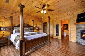 A wooden cabin-style bedroom with a four-poster bed, a fireplace, and a ceiling fan.