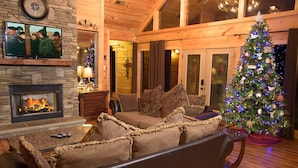A cozy living room with a fireplace, a television mounted on the wall, a Christmas tree, and a comfortable sofa. - Gatliburg Mansion | Best Views In The Smokies | 14 Full Suites (Gatlinburg)