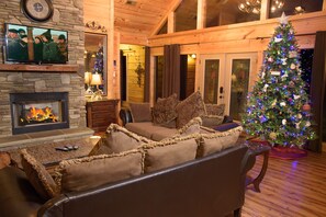 Un salon chaleureux avec une cheminée, un téléviseur fixé au mur, un sapin de Noël et un canapé confortable.