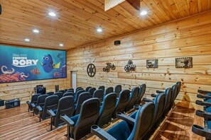 A cozy cinema room with wooden walls and ceiling, rows of black seats, and a large screen displaying 'Finding Dory'.