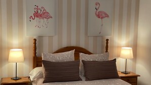 A hotel room with a bed, two nightstands, two lamps, and two framed pictures of flamingos on the wall. - Centeno rural house, Terrace, BBQ Garden, Fireplace, wifi, Hayedo Montejo (Montejo de la Sierra)