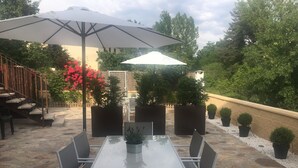 An outdoor patio with a stone floor, a glass table with metal chairs, and large umbrellas providing shade. - Centeno rural house, Terrace, BBQ Garden, Fireplace, wifi, Hayedo Montejo (Montejo de la Sierra)