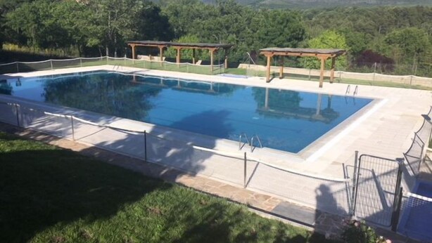 A rectangular swimming pool with a wooden deck and pergola structures, surrounded by a fence and set against a backdrop of trees and mountains. - Centeno rural house, Terrace, BBQ Garden, Fireplace, wifi, Hayedo Montejo (Montejo de la Sierra)