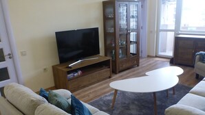 Un salon avec un téléviseur à écran plat posé sur un meuble en bois, une vitrine, une table basse blanche et un canapé beige.