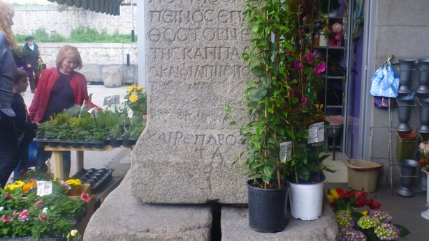 Un monument de pierre orné d’inscriptions, entouré de plantes et de fleurs en pot.