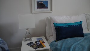 A neatly arranged bedroom with a bed, a bedside table with a lamp, and a framed picture on the wall.