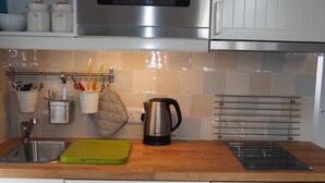A kitchen with stainless steel appliances, a sink, and a countertop with various utensils and a kettle.