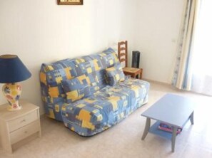 A living room with a blue and yellow patterned sofa, a small wooden chair, a table, and a lamp. - Studio on on a flowered land of 3000 square meters, view on the mountain (Calvi)