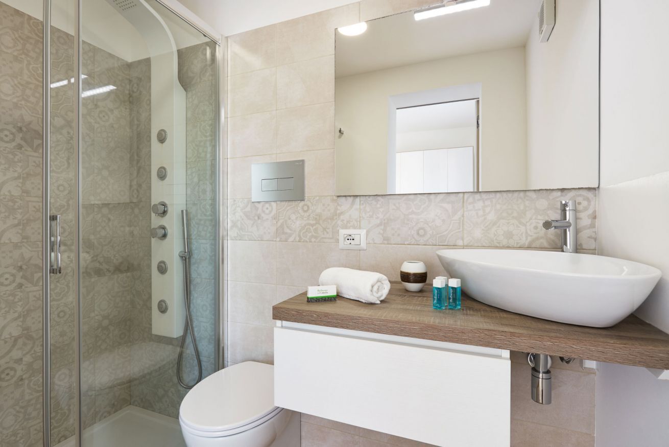 A modern bathroom with a glass shower enclosure, a white toilet, a sink with a wooden countertop, and a mirror above the sink.