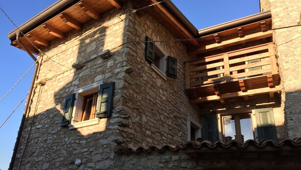 Un bâtiment en pierre avec des poutres et des volets en bois, doté d’un balcon et d’une petite fenêtre.