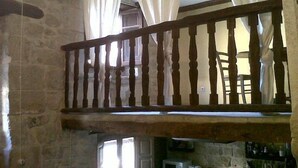 Un intérieur rustique en pierre, agrémenté d’une balustrade en bois, d’un mur de pierre et d’une fenêtre avec des rideaux.