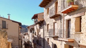 Une ruelle étroite pavée, bordée de bâtiments en pierre dotés de balcons et de portes en arc de cercle.