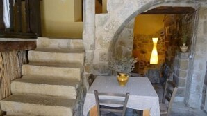 Un escalier en pierre mène à une pièce où se trouvent une table et des chaises, une lampe et un vase.