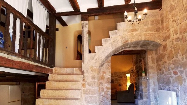 Un escalier en pierre menant à un deuxième étage, avec une rampe en bois et un lustre.