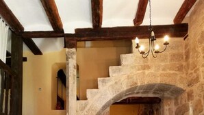 Un escalier en pierre mène à une salle à manger en bois, surmontée d’un lustre.