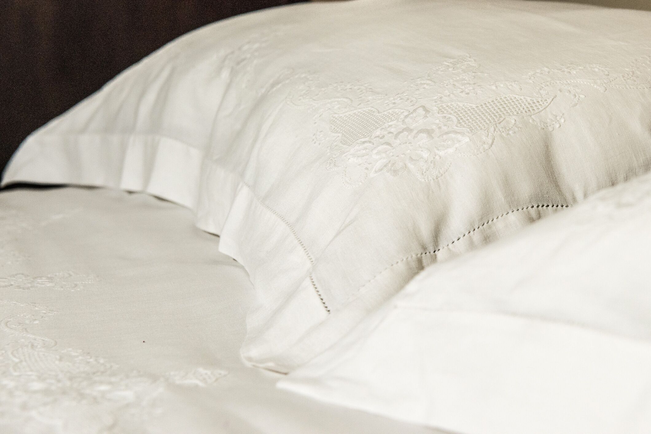 A close-up of a bed with a white, textured bedspread and pillows.