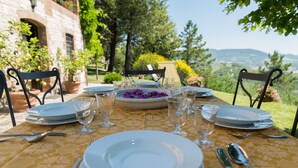 A table set for a meal with plates, glasses, and cutlery, surrounded by chairs, in a garden with a view of hills. - CHARMING FARMHOUSE IN THE MARCHIGIAN HILLS (Fabriano)