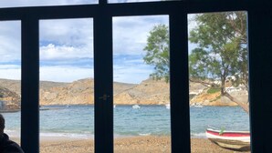 Blick durch ein Fenster auf einen Strand und Boote im Hintergrund.