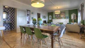 A spacious dining area with a wooden table and green chairs, a kitchen with a green accent wall, and a fireplace. - 30 guests Upper Class (Lisboa)