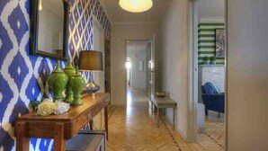 A hallway with patterned wallpaper, a wooden console table with decorative items, and a hanging light fixture. - 30 guests Upper Class (Lisboa)