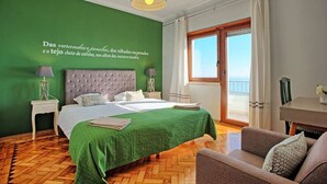 A hotel room with a green wall, a large bed with a green bedspread, two bedside tables with lamps, a wooden floor, a balcony with curtains, and a view of the sea. - APOLONIA 4 FRONTAL. In the center of the monumental Lisbon  (Lisboa)