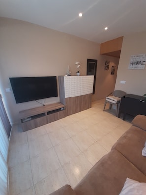 A living room with a flat-screen TV, a wooden cabinet, a brown sofa, and a small table with a plant.