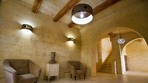 A spacious room with a high ceiling, exposed wooden beams, and a stone wall. There are two armchairs and a small table with a decorative item. A staircase leads to an upper level. - Amazing views, complete privacy, luxury and comfort including pool and deck area (Ghasri)