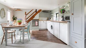 Eine kleine Küche mit einem Holztisch, Stühlen, einer Waschmaschine und einer Mikrowelle.