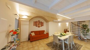 A living room with a sofa, a dining table with chairs, a staircase, and a wall with artwork. - Cozy and comfortable apartment in Matera (Matera)