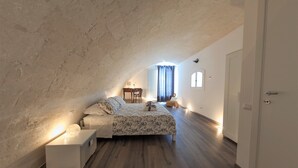 A bedroom with a sloped ceiling, a bed with a floral bedspread, a bedside table, and a lamp. - Cozy and comfortable apartment in Matera (Matera)