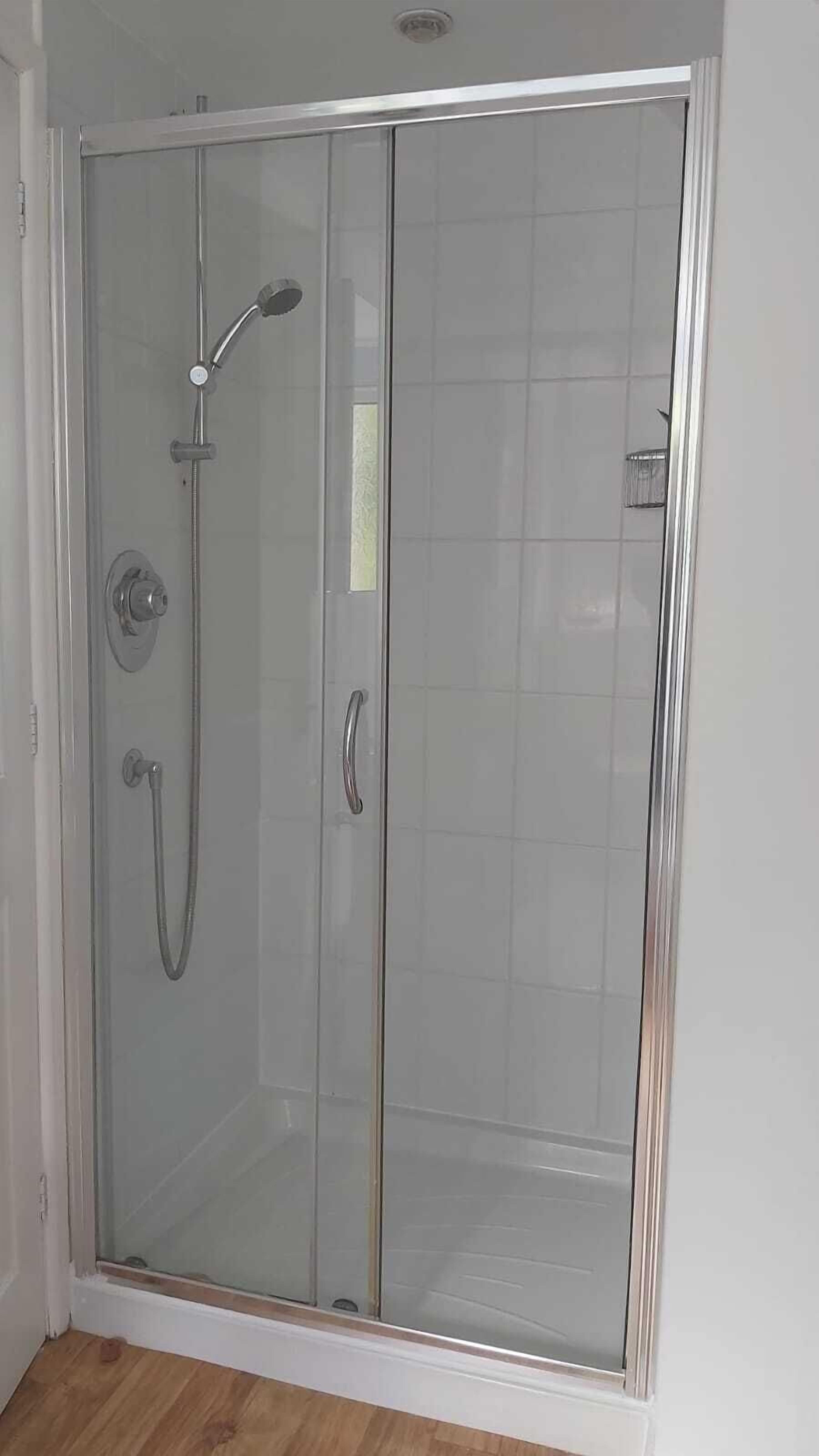A glass-enclosed shower stall with a handheld showerhead and a handheld shower attachment.