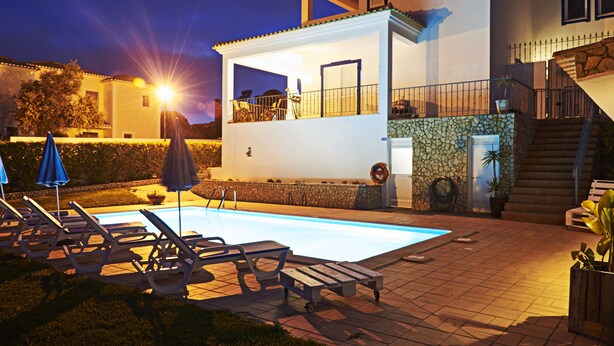 Una casa de dos pisos con piscina, mobiliario exterior y una escalera.
