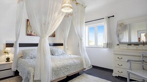 Un dormitorio con cama a dosel, cómoda, espejo y ventana con cortinas.