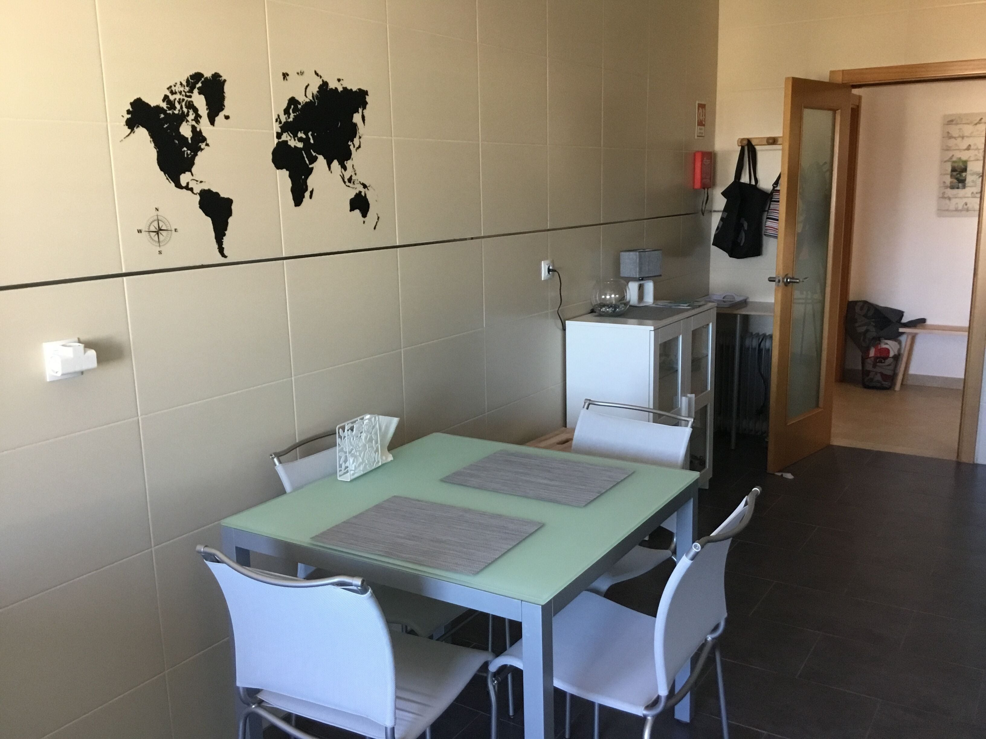 Un comedor con una mesa y sillas, un mapa del mundo en la pared, un mueble pequeño y una puerta que da a otra habitación.