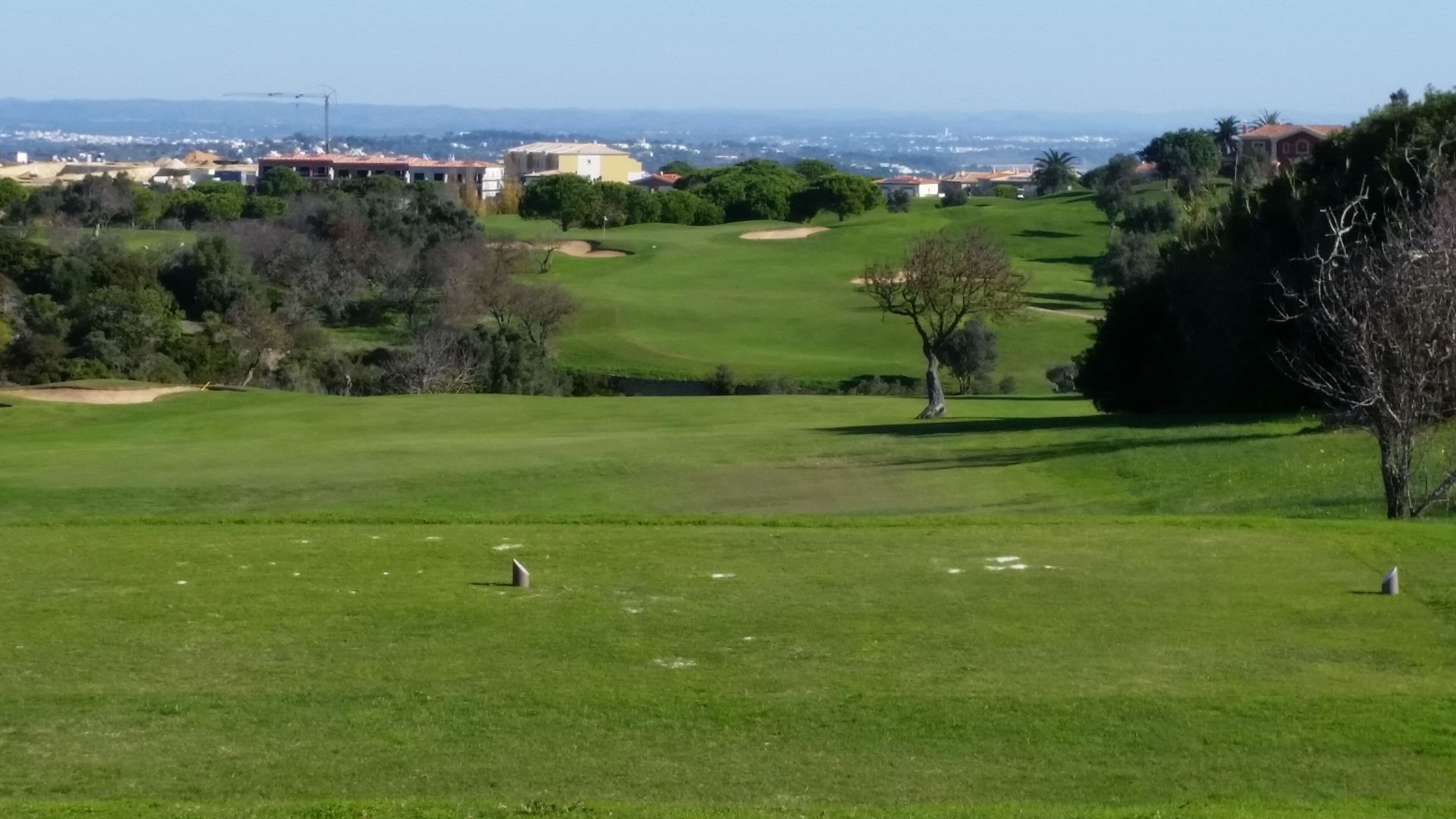 Un parcours de golf offrant une vue dégagée sur le fairway, les bunkers de sable et une ville située au loin.