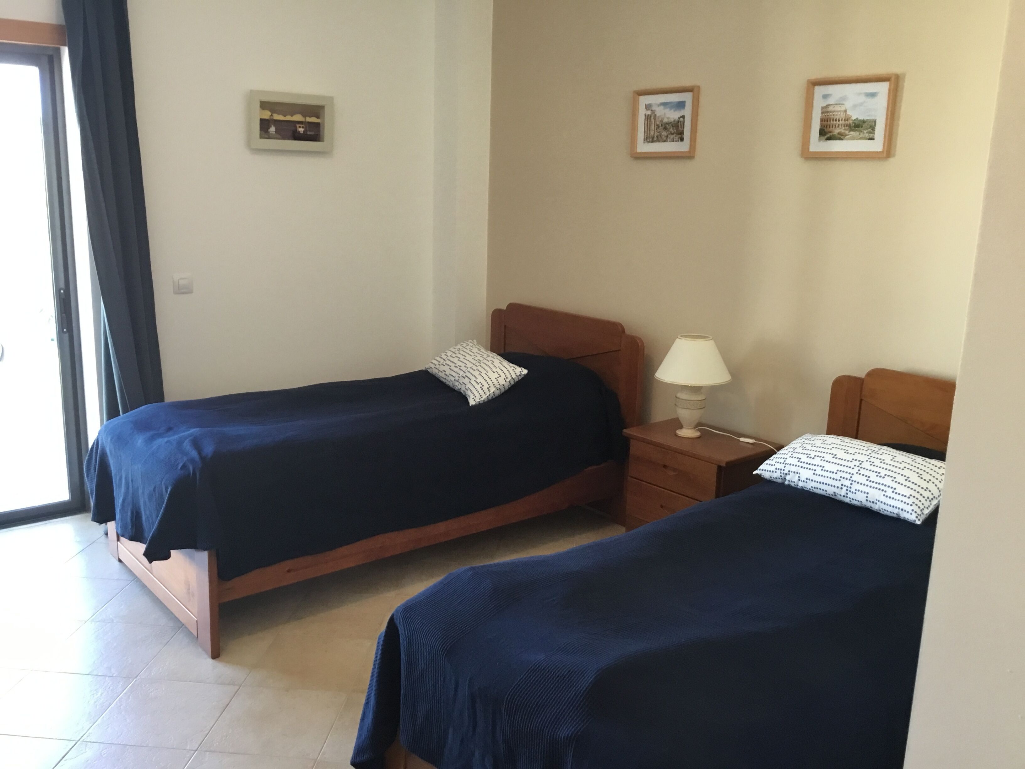 Ein Zimmer mit zwei Einzelbetten, einem Nachttisch mit Lampe und zwei gerahmten Bildern an der Wand.