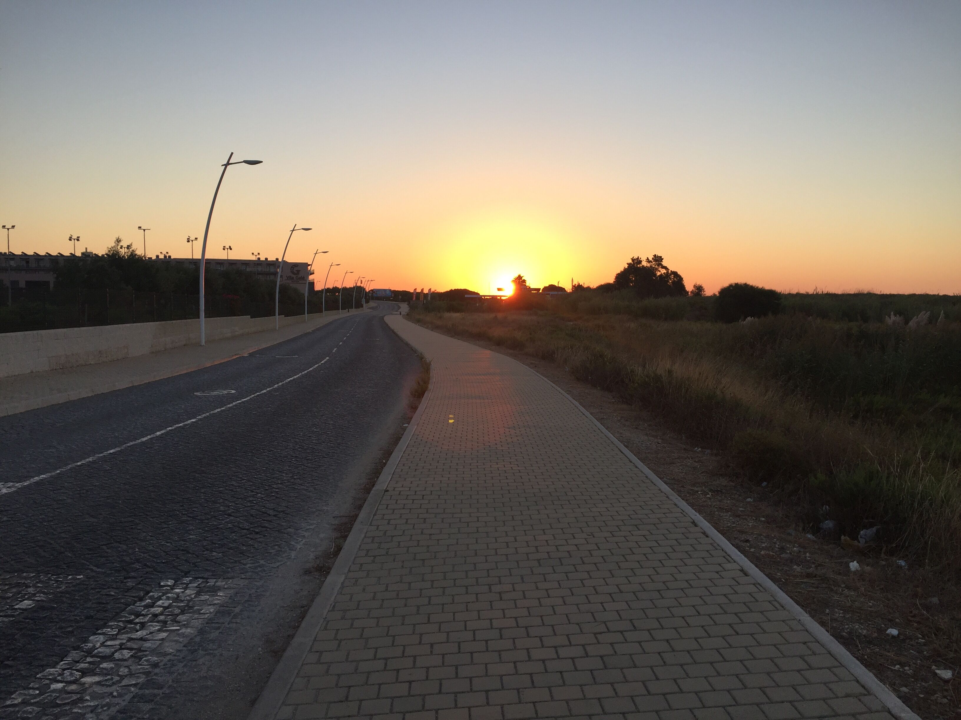 Una carretera pavimentada con acera, que se extiende hacia un atardecer.