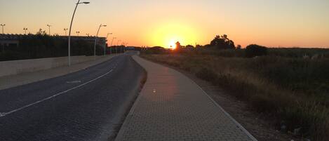 Una carretera pavimentada con acera, que se extiende hacia un atardecer.