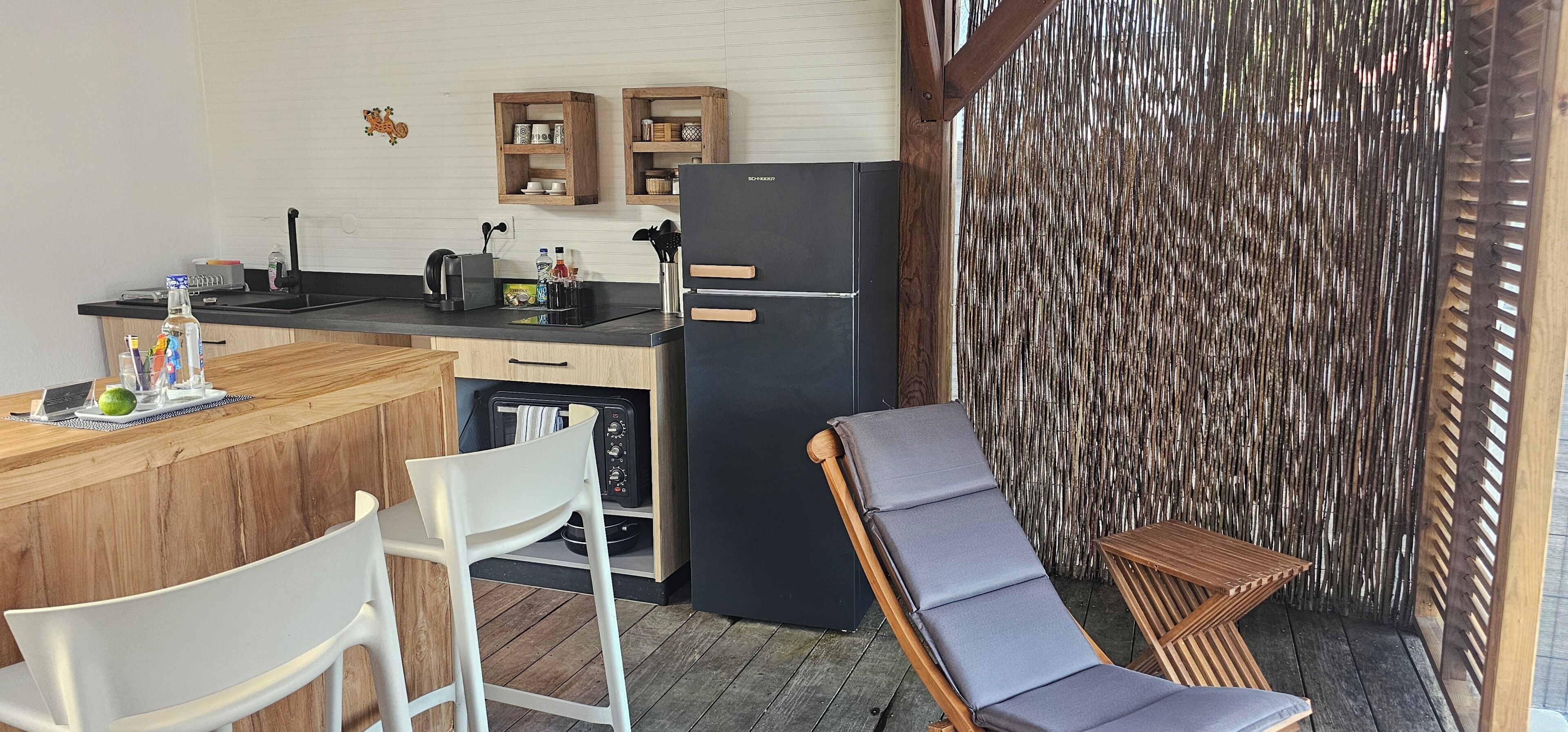 A compact kitchen with a refrigerator, wooden cabinets, and a bar area. There is a seating area with a chair and a table.