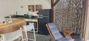 Une cuisine compacte équipée d’un réfrigérateur, de meubles en bois et d’un coin bar. Un espace détente avec une chaise et une table est également prévu.